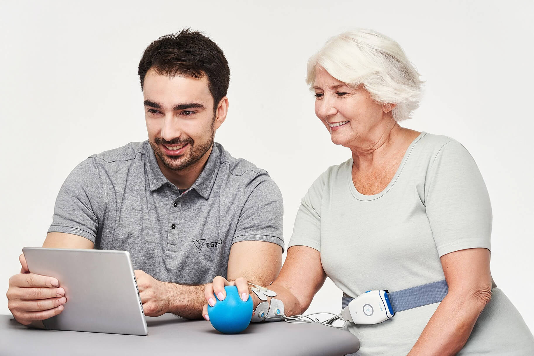 Physiotherapie zu Hause: Therapeut mit älterer Frau und Tablet. Rehabilitation.